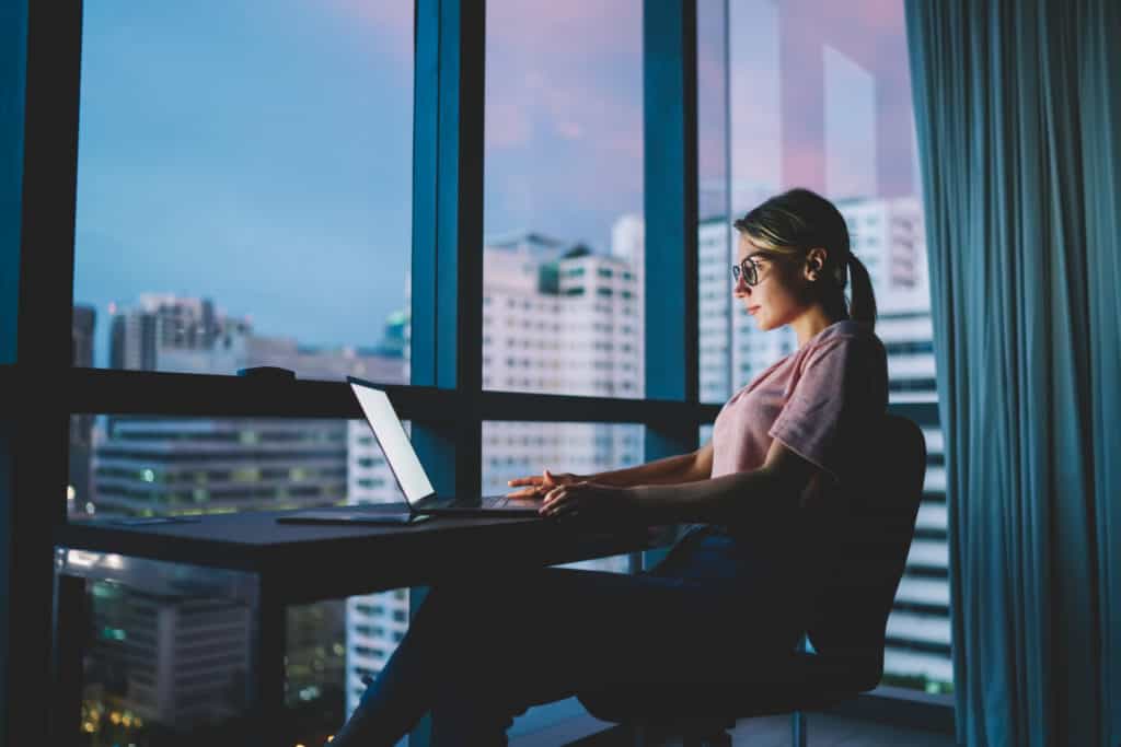 woman-in-office-highrise-sitting-at-table-with-laptop-loading-website