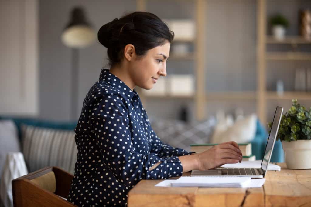 young-business-woman-in-profile-sitting-at-desk-while-working-on-laptop-studying-seo-trends-in-2021