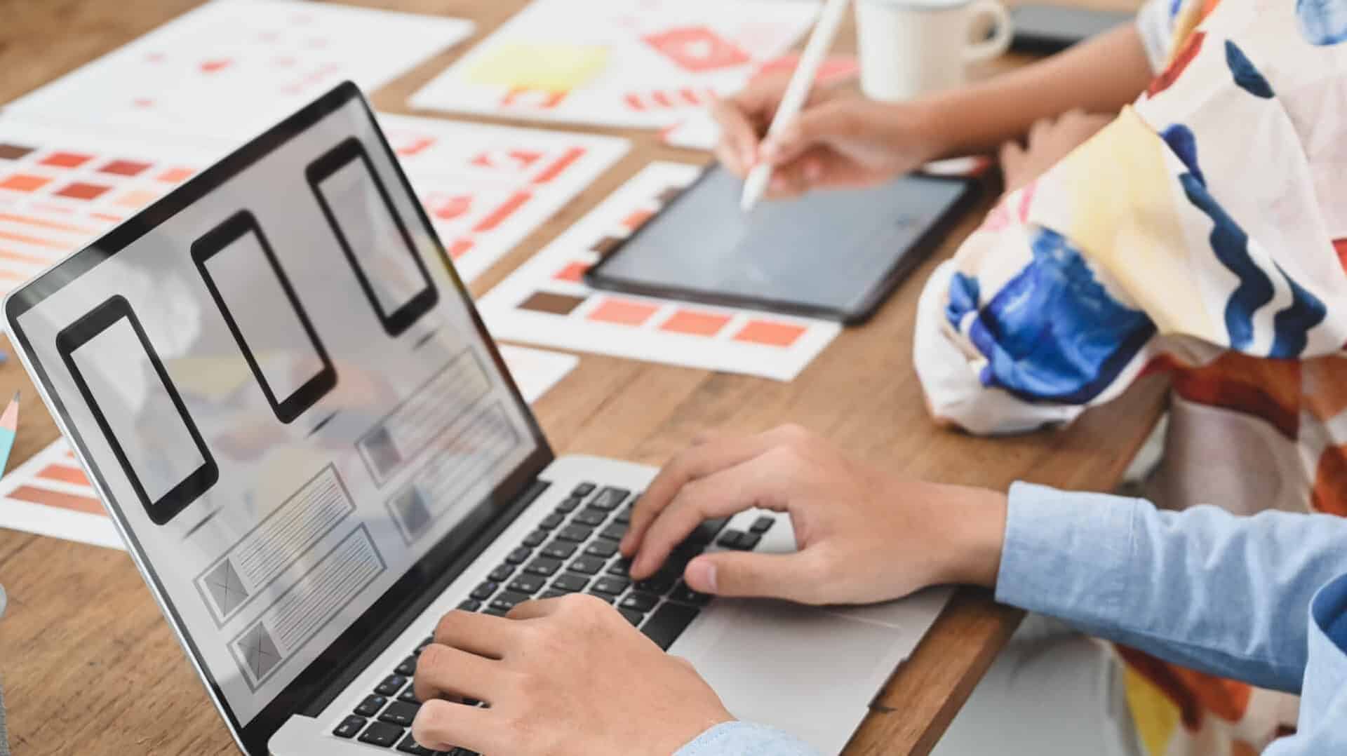 two-people-working-on-website-landing-page-mobile-design-at-desk-with-laptop-and-tablet