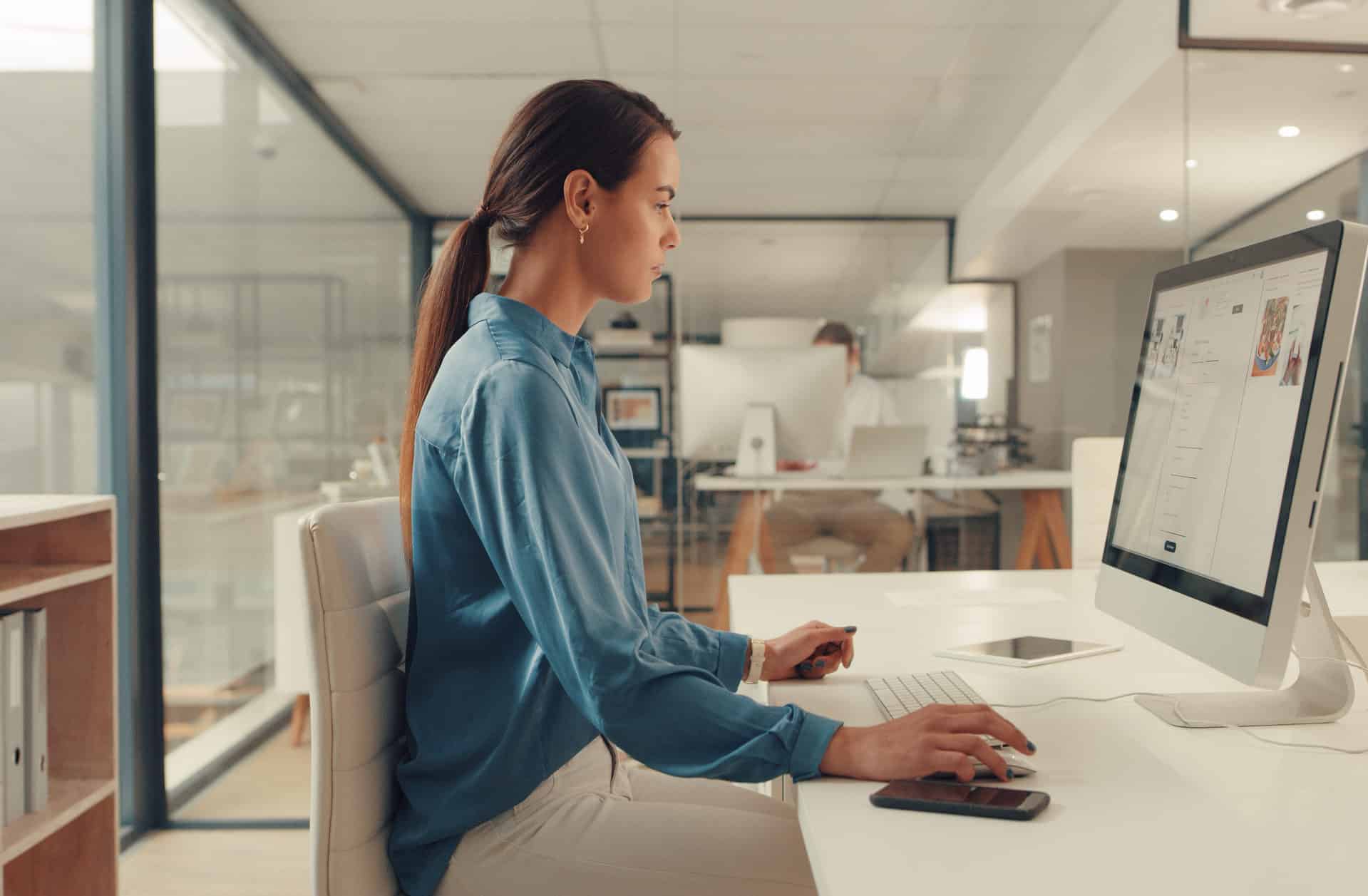 A woman in profile sitting at a desk and working on image SEO on a computer monitor with a mouse and keyboard.